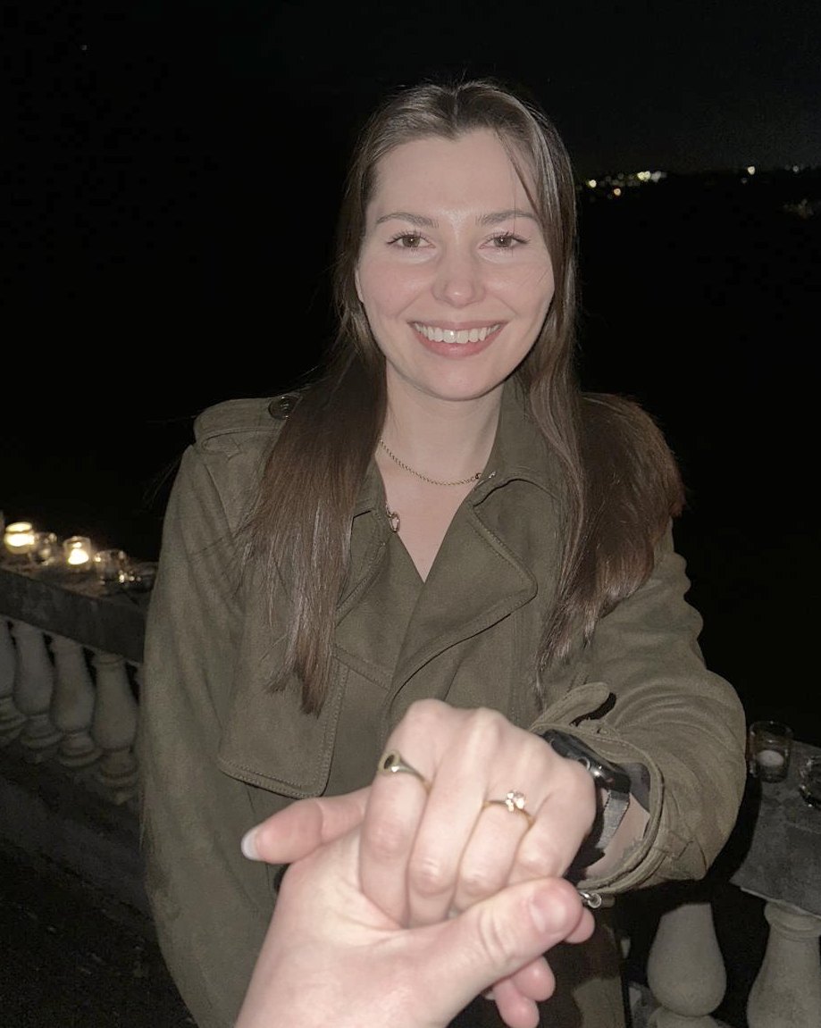 Lee-Anne smiling on a candlelit terrace at night, holding out her hand with the engagement ring